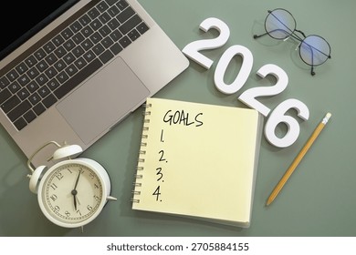 flat-lay of open notebook labeled “Goals” with lists of thing to do, number of New Year 2026, pencil, laptop, alarm clock and eyeglasses on green desk. goal setting, planning for New Year concept - Powered by Shutterstock - Get 15% off with code: PIKWIZARD15