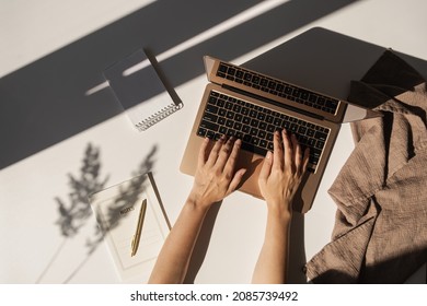 Flatlay of person hands working on laptop computer. Aesthetic bohemian home office workspace. Work at home. Notebook, pampas grass sunlight shadow on table. Flat lay, top view
