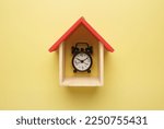 A flatlay picture of house miniture with alarm clock on yellow background.