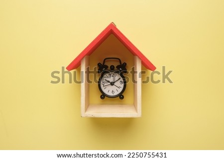 A flatlay picture of house miniture with alarm clock on yellow background.