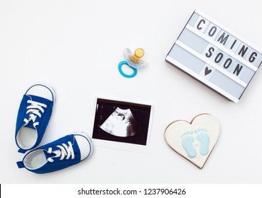 flatlay pregnancy composition with space for text on white background. top view of children's accessories: toys, pacifier, baby screen, baby projector lamp "coming soon" and delicious gingerbread
