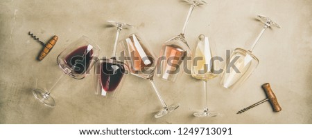 Flat-lay of red, rose and white wine in glasses and corkscrews over grey concrete background, top view, wide composition. Wine bar, winery, wine degustation concept