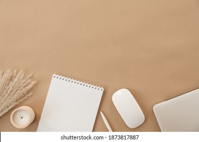 Flatlay of spiral flip notebook with blank paper sheet. Laptop, pampas grass, stationery on beige peachy pastel background table. Minimalist home office desk workspace. Top view mockup copy space.