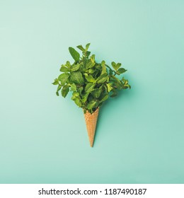 Flat-lay of sweet waffle ice-cream cone with bunch of fresh green mint over pastel mint background, top view, square crop. Spring or summer mood concept Stock-foto