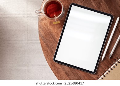 Flatlay of a tablet blank screen on wooden table with tea and notebook. Tablet screen is blank. Tea cup beside tablet. Notebook and pen near tablet. Cozy workspace setup. - Powered by Shutterstock