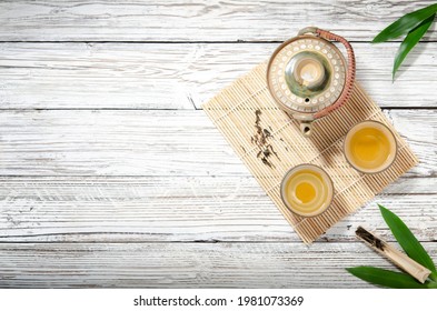 Flatlay Or Top View Hot Tea From A Teapot In A Cup,  Japanese Style And Leaves On The Old White Wood Table. Left Side Copy Space, Suitable For Creative Graphic Design.