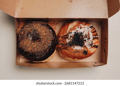 Flatlay top view of two doughnuts with chocolate and tiramisu flavor inside a box.
