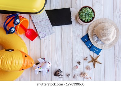 Flatlay Travel Top View. On White Wooden Background Lie Plane Tickets, Passports, Map, Seashells, Yellow Suitcase, Inflatable Rubber Duck, Swimming Goggles, Hat, Shovel, Bucket. Vacation With Children