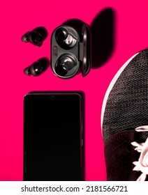 Flatlay Of True Wireless Earphones Running Shoe And Phone Playing Music Against Bright Pink Background