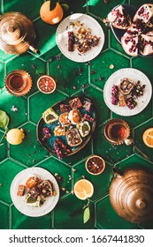 Flat-lay of variety of Turkish traditional lokum sweet delight with Turkish tea in copper pots and tulip glasses over green Moroccan tile table, top view. Middle East typical dessert food