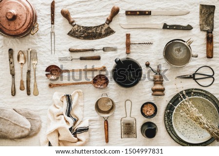 Flat-lay of various kitchen utensils, rustic tablewear, plates, dishes, glasswear, pan, scissors, corkscrew, textile for cooking over white linen tablecloth background, top view. Seasonal cooking