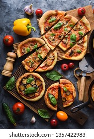 Flatlay of vegetarian pizza party. Homemade rustic pizzas with tomatoes, mushrooms, bell peppers, eggplants and basil on dark background