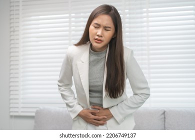 Flatulence, abdomen asian young business woman in suit at home, hand in stomach ache, expression face suffer from food poisoning, abdominal pain and colon problem, gastritis or diarrhoea, inflammation - Shutterstock ID 2206749137
