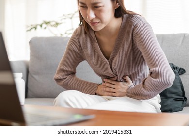 Flatulence asian young woman hand in stomach ache suffer from food poisoning, gastritis or diarrhoea, pain belly, abdomen or inflammation, use laptop computer consulting with doctor online at home. - Shutterstock ID 2019415331