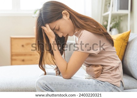Flatulence asian young woman intolerance hand in stomach ache, suffer from food poisoning, abdominal pain and colon problem, gastritis or diarrhoea when at home. Patient belly, abdomen or inflammation