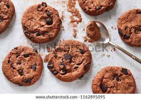Flatview of handcrafted chocolate cookies with chocolate chips and tea spoon with cocoa powder on baking paper. Natural handmade organic snakes for healthy breakfast