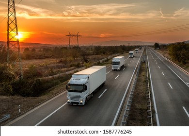 Fleet Of Blue Lorry Trucks On A Country Highway Under An Amazing Orange Sunset Sky