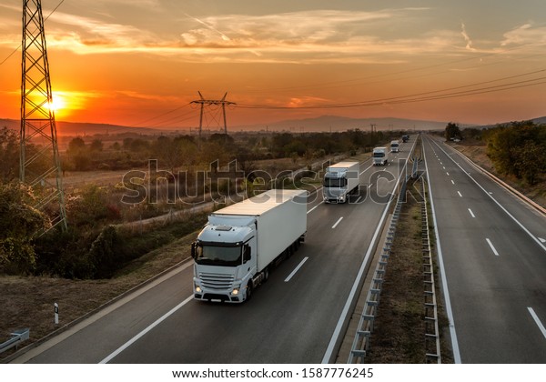 Fleet of blue lorry trucks on a country\
highway under an amazing orange sunset\
sky