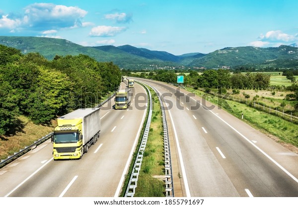 Fleet or Convoy of big\
transportation trucks in line  on a countryside highway under a\
blue sky