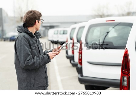 Fleet manager with digital tablet supervising rows of white delivery vans