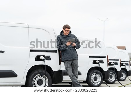 Fleet manager with digital tablet supervising rows of white electric delivery vans	
