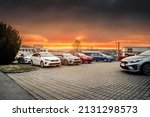 Fleet of modern new stock vehicles standing in the parking lot prepared for carsale during cloudy morning sunrise. Row of cars with different colors and sizes waiting for new customers.