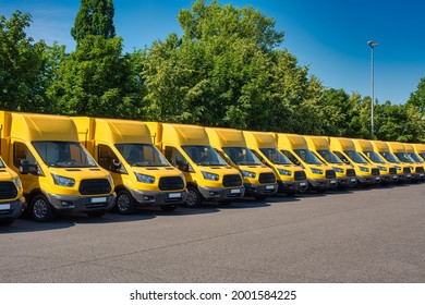 A fleet of yellow electric delivery vans parking in front of green trees.