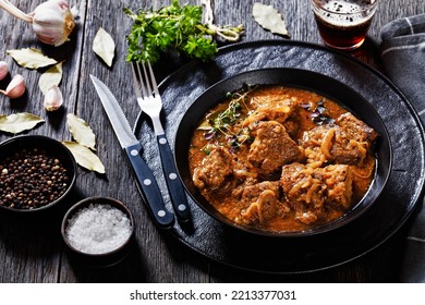 Flemish Stew, stoofvlees, carbonnade, beef or pork, beer and onion stew in black bowl on dark rustic wooden table with glass of beer