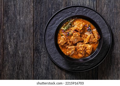 Flemish Stew, stoofvlees, carbonnade, beef or pork, beer and onion stew in black bowl on dark wood table, horizontal view from above, flat lay, free space