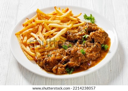 Flemish Stew, stoofvlees, carbonnade, beef or pork, beer and onion stew with french fries on white plate on wood table, landscape view