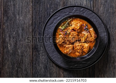 Flemish Stew, stoofvlees, carbonnade, beef or pork, beer and onion stew in black bowl on dark wood table, horizontal view from above, flat lay, free space