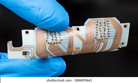 Flex printed circuit board with copper layer in man fingers isolated on black background. Detail of hand in blue glove holding white PCB sheet with integrated connector for computer printer printhead.