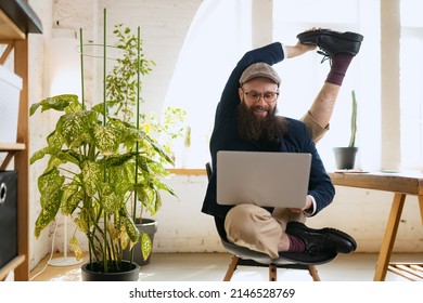 Flexibility. Man practicing yoga. Young bearded office clerk having fun, doing yoga on wooden table in modern office at work time with gadgets. Concept of business, healthy lifestyle, sport, hobby