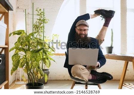 Flexibility. Man practicing yoga. Young bearded office clerk having fun, doing yoga on wooden table in modern office at work time with gadgets. Concept of business, healthy lifestyle, sport, hobby