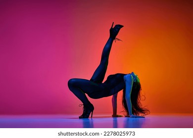 Flexibility. Young woman, professional dancer performing high heel dance over gradient red pink studio background in neon light. Concept of contemporary dance style, art, aesthetics, hobby, creativity