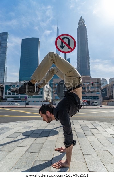 Flexible Acrobat keep balance on\
the hands with blurred Dubai cityscape and traffic sign U-Turn is\
prohibited. Concept of modern, business and unlimited possibility\
