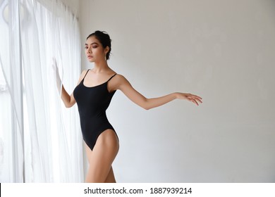 Flexible Asian Ballet Dancer Stretching On White Wall Studio