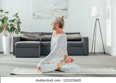 flexible athletic man practicing yoga on mat at home