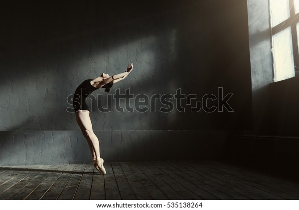 Flexible ballet dancer stretching in the dark\
lighted studio
