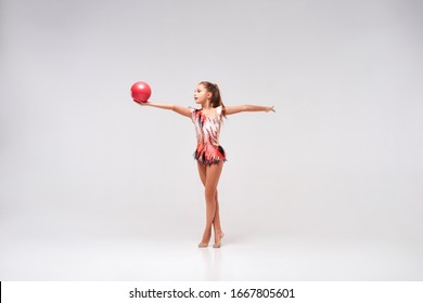 Flexible cute little girl child gymnast doing acrobatic exercise using ball isolated on a white background. Sport, training, active lifestyle concept. Horizontal shot