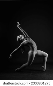 Flexible girl, rhythmic gymnastics artist jumping on white dark background. Grace in motion, action. - Shutterstock ID 2303801295