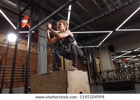 flexible, muscular sporty woman performing jump squats in the fitness center to keep fit. side view full length photo