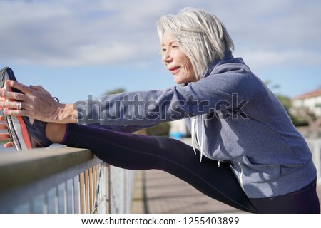  Flexible senior woman stretching outdoors after jog                              