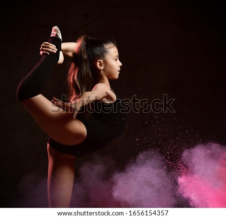 Flexible skinny girl posing in vertical split . Balance on one leg with a grip. Sports concept, gymnastics, fitness. on a dark background with pink smoke.