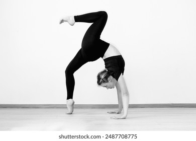 Flexible, slender girl gymnast in a bridge pose on a white background. Gymnastics and yoga classes in the studio. Black and white artistic photo. High quality photo - Powered by Shutterstock