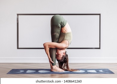 Flexible slim young woman acrobat. Head to knees, uttanasana exercise, Standing forward bend pose. Concept of flexible joints and slim body. Urdhva mukha paschimottanasana exercise. Yoga white class