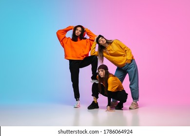 Flexible. Sportive Girls Dancing Hip-hop In Stylish Clothes On Colorful Gradient Background At Dance Hall In Neon Light. Youth Culture, Movement, Style And Fashion, Action. Fashionable Portrait.