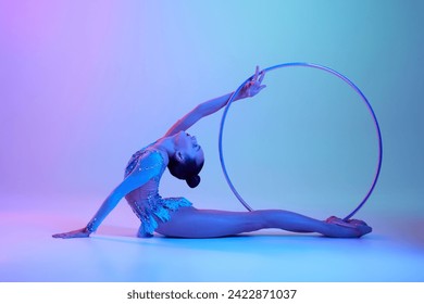 Flexible, talented teen girl, rhythmic gymnast in sparkling bodysuit performing with hoop against gradient studio background in neon light. Concept of sport, grace, competition, art, youth, hobby - Powered by Shutterstock