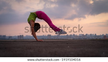Flexible woman doing handstand outdoor on the dramatic sunset background. Concept of yoga, healthy lifestyle and individuality
