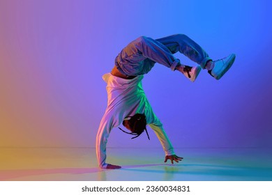 Flexible young man, contemp dancer performing breakdance, hip-hop against gradient multicolored studio background in neon light. Concept of street style dance, fashion, youth, hobby, dynamics, ad - Powered by Shutterstock